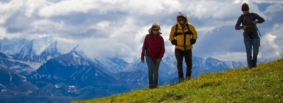 Three people hiking on a grassy hill with mountains in the background
